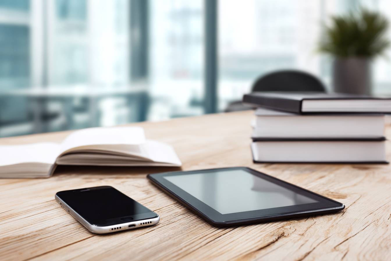 Tablet, Smartphone und Bücher auf einem Holztisch in einem modernen Büro.